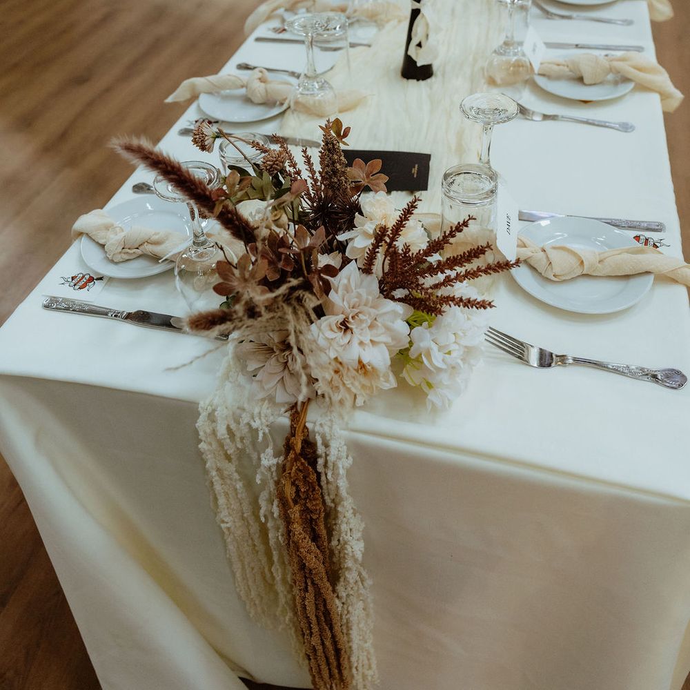 Long banquet table with dahlias, dried grasses and taper candles cascading over the edge