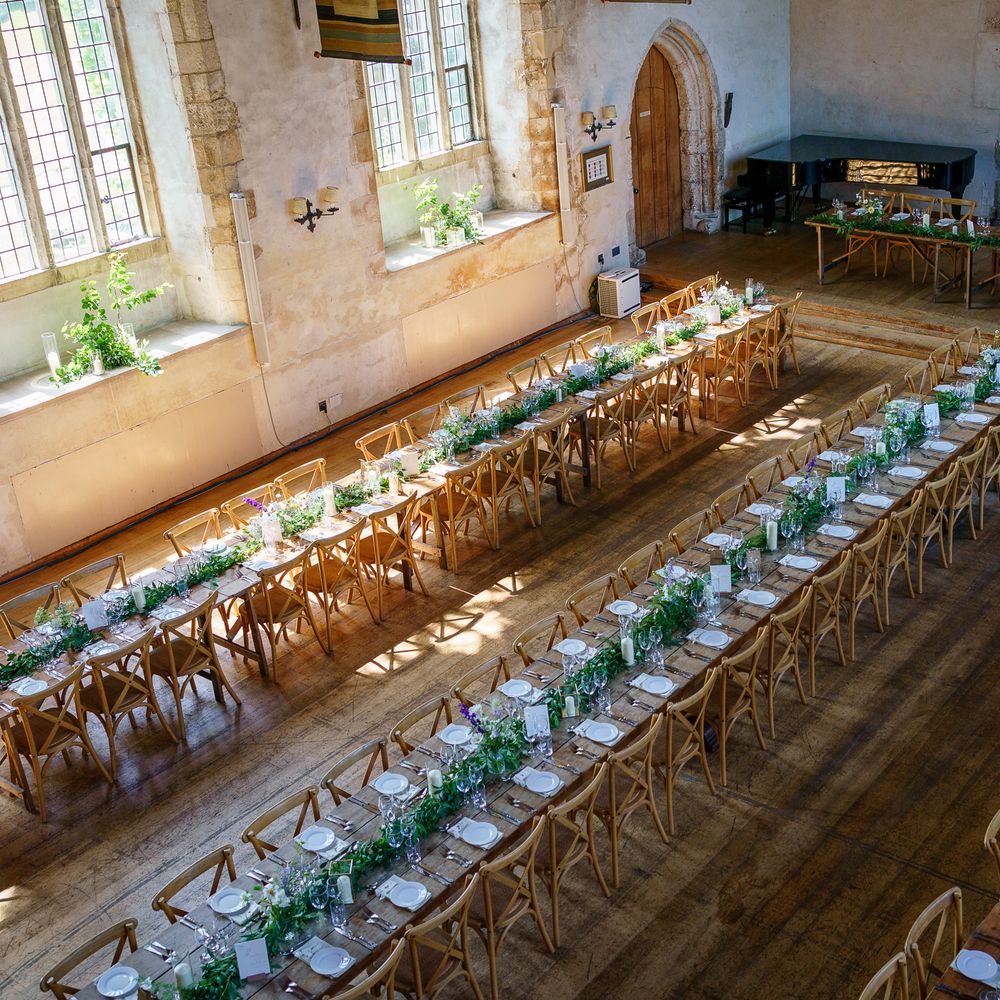 Long banquet tables with foliage runners and cross-back chairs in a historic stone hall