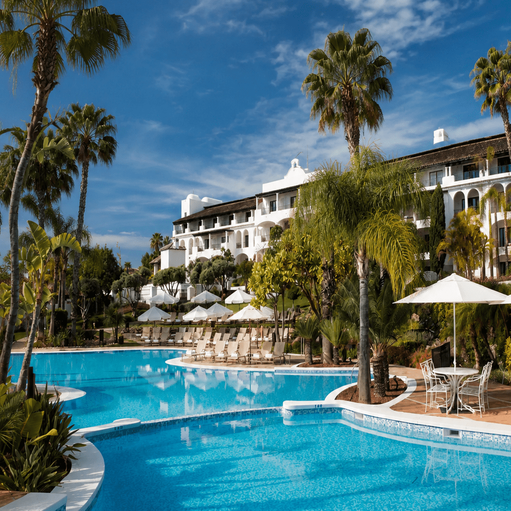 Luxury resort swimming pool with palm trees, sun loungers and Mediterranean-style hotel