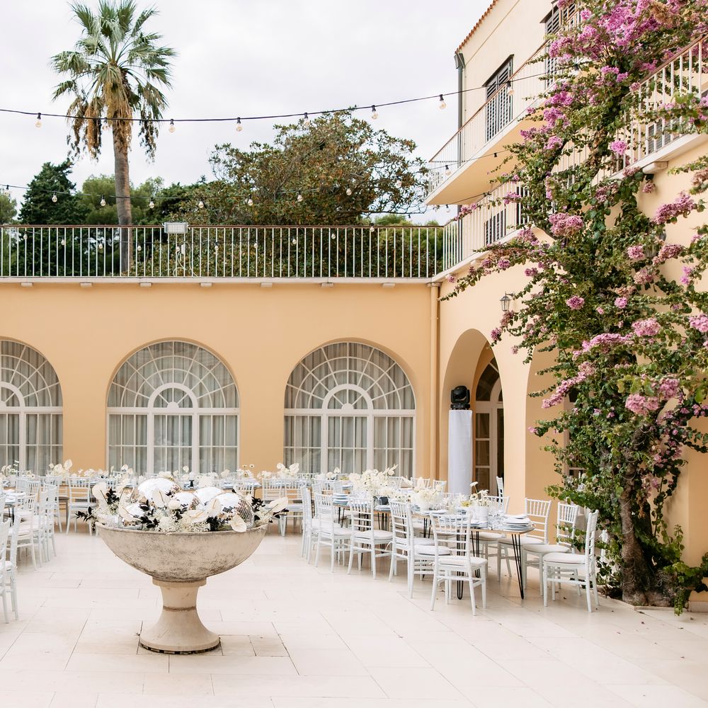 Mediterranean courtyard set for a wedding reception with white chairs and floral centrepieces