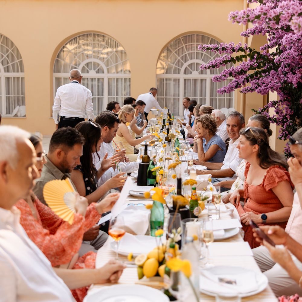 Guests seated at a long outdoor table with lemons and yellow blooms beneath pink bougainvillea