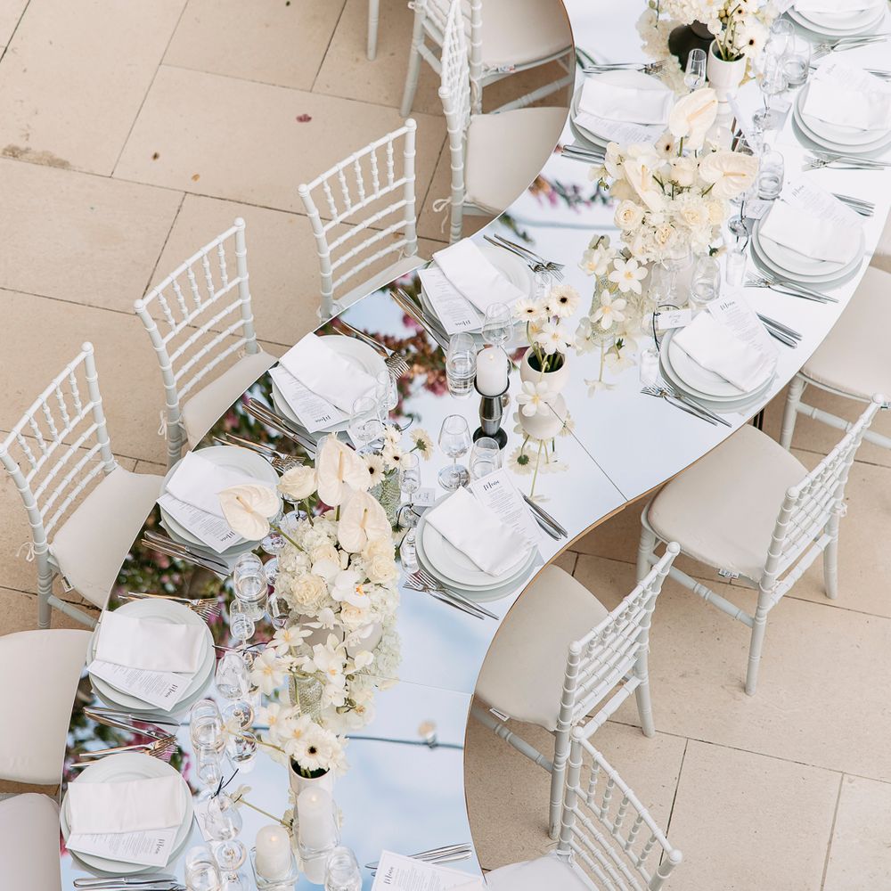 Curved mirrored wedding table with white chiavari chairs and ivory floral centrepieces outdoors