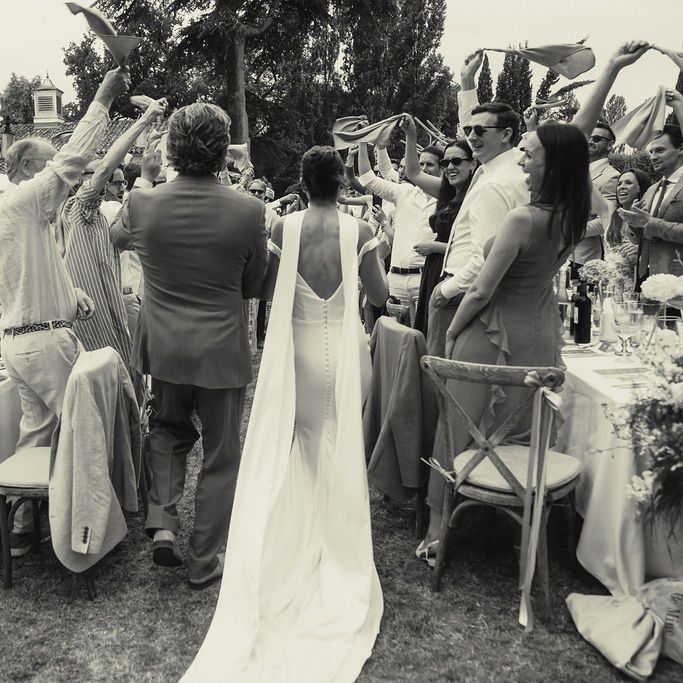 Bride and groom walk between guests waving napkins at an outdoor reception
