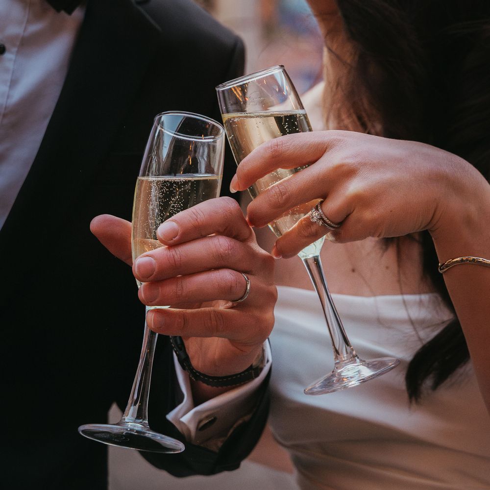 Newlywed couple kiss while holding champagne flutes, the groom in black tie and bride in white