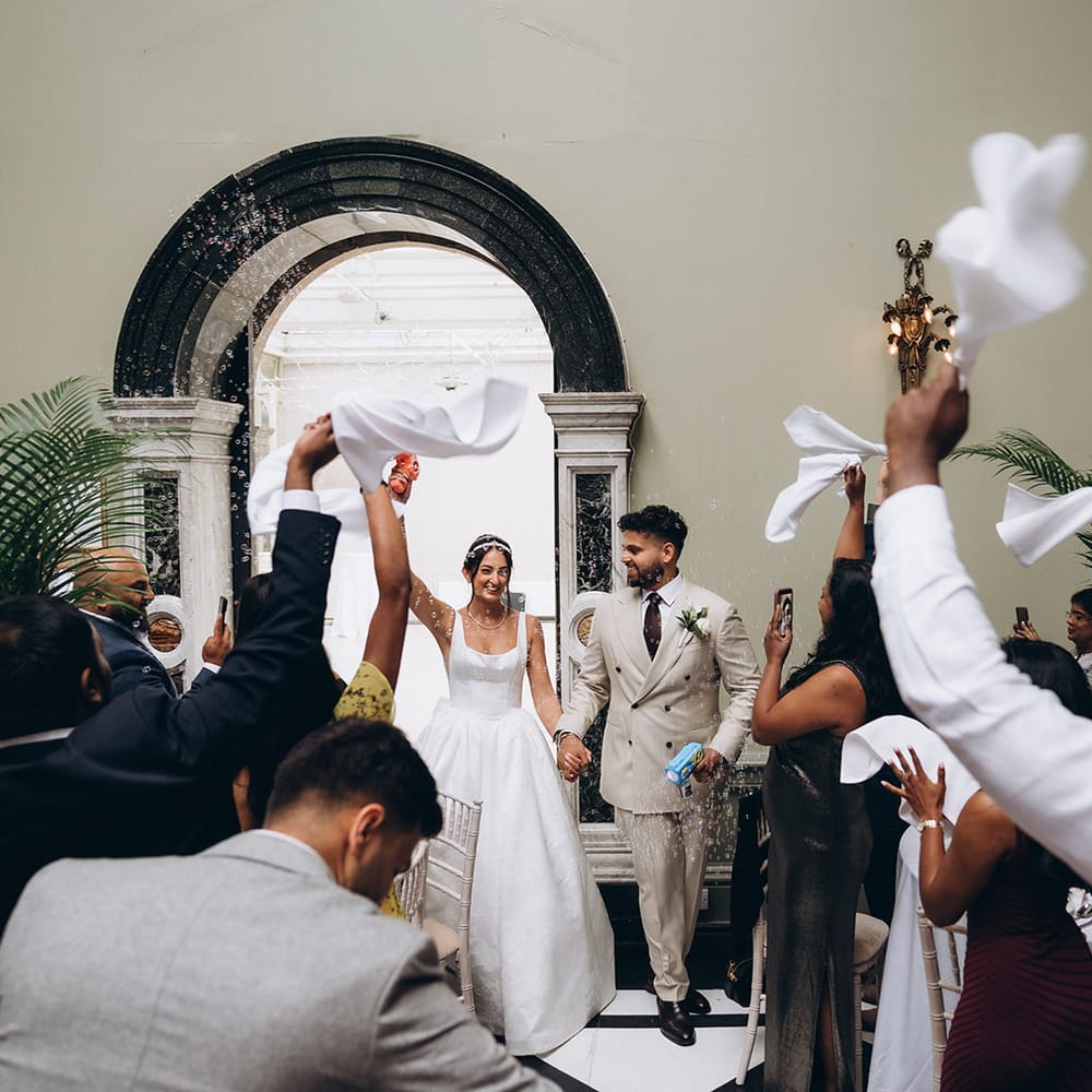 Newlyweds hold hands as guests wave white napkins to celebrate after the ceremony