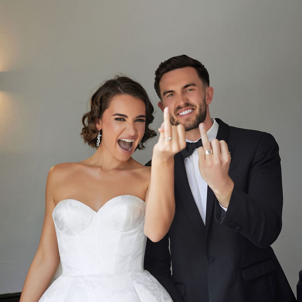 Laughing newlyweds hold up their hands to show off their wedding rings after saying I do