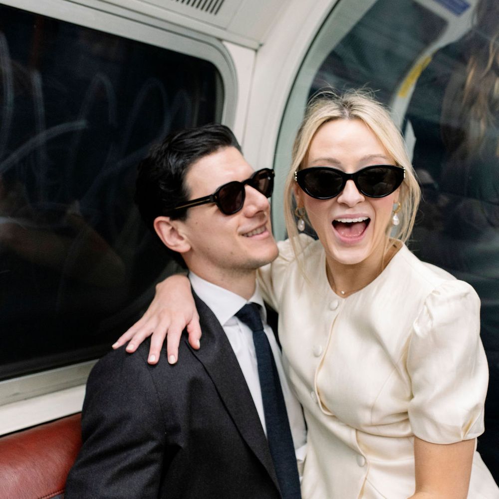 Newlywed couple in sunglasses laughing on a London Underground train seat