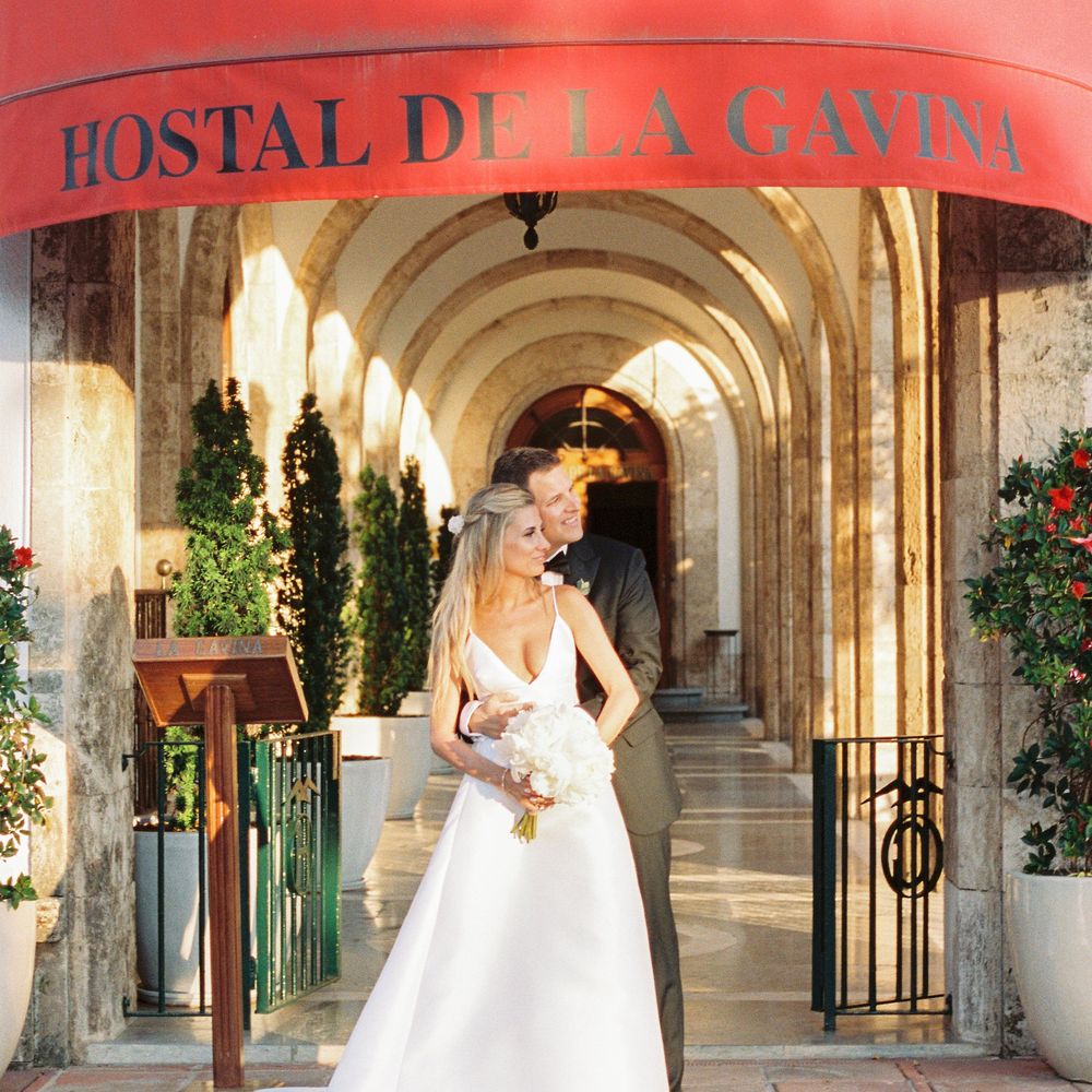 Bride and groom embracing beneath a red awning at an arched stone entrance