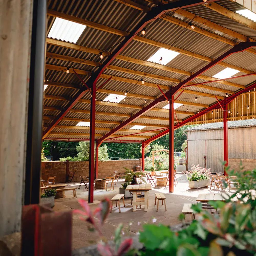 Open-sided barn with red steel beams, festoon lights and wooden tables set for an outdoor reception