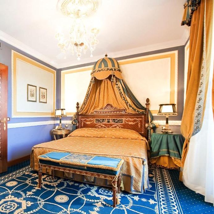 Opulent hotel suite with canopied bed, gilded chest of drawers and blue patterned carpet