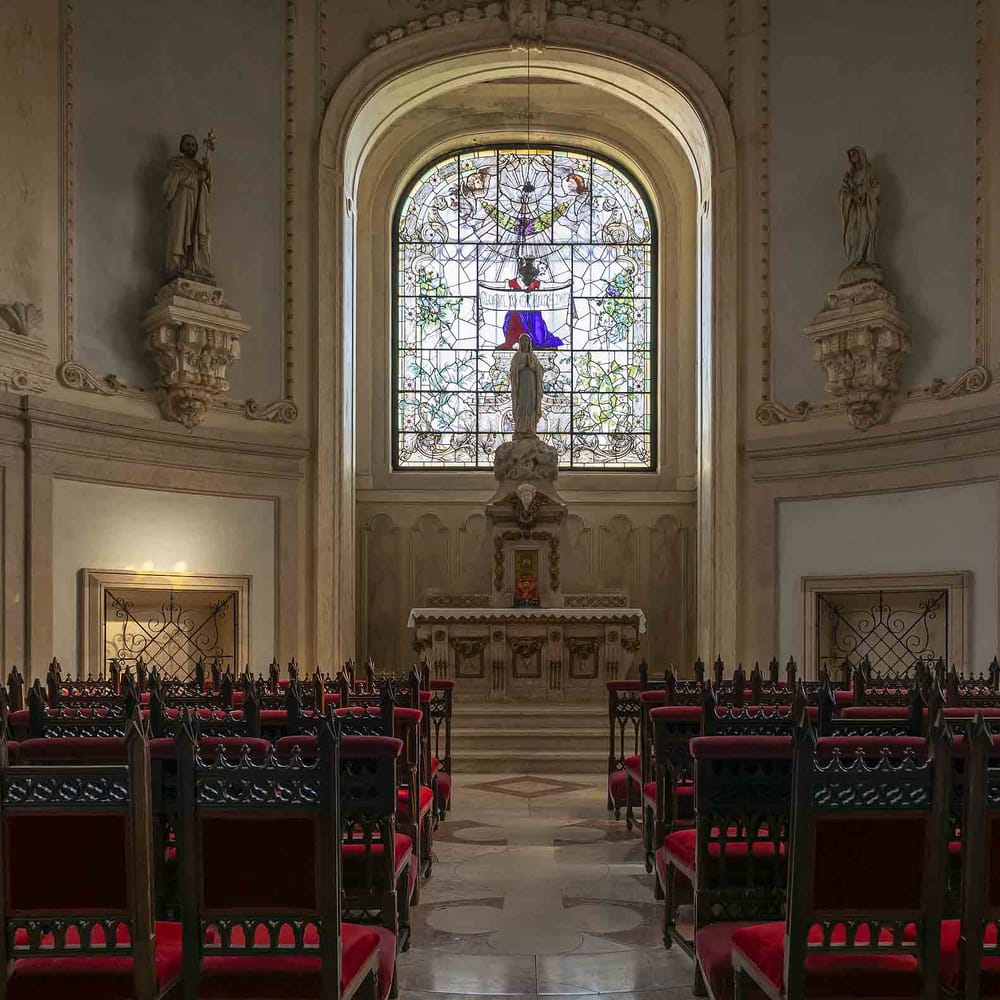Ornate chapel interior with stained glass windows, carved wooden chairs and a marble altar