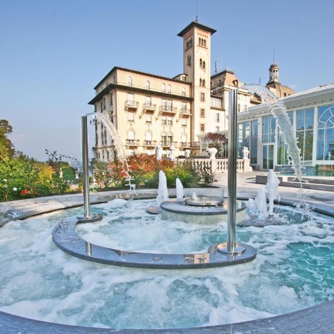 Outdoor water feature and hydrotherapy pool with jets before a grand historic hotel and glass conservatory.