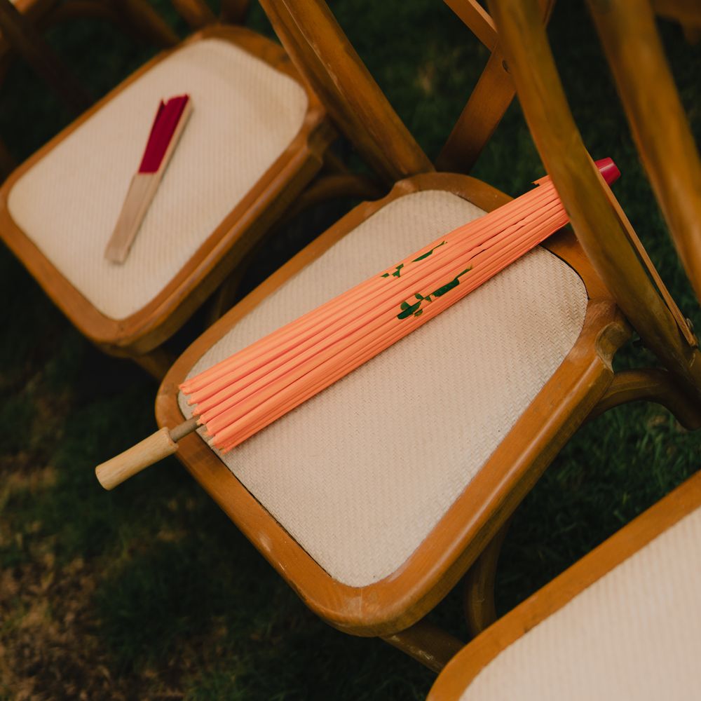 Coral paper parasols resting on wooden crossback chairs on a grass lawn