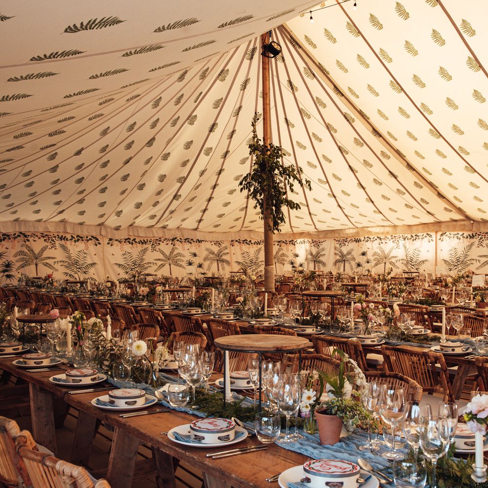 Patterned marquee interior with wooden trestle tables, foliage runners and terracotta potted plants