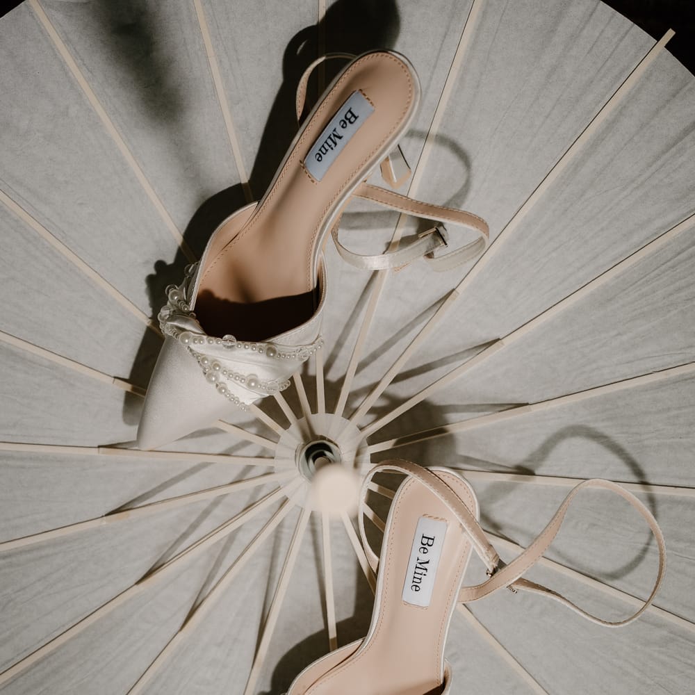 Pearl-embellished Be Mine bridal heels arranged on a white paper parasol in dappled light