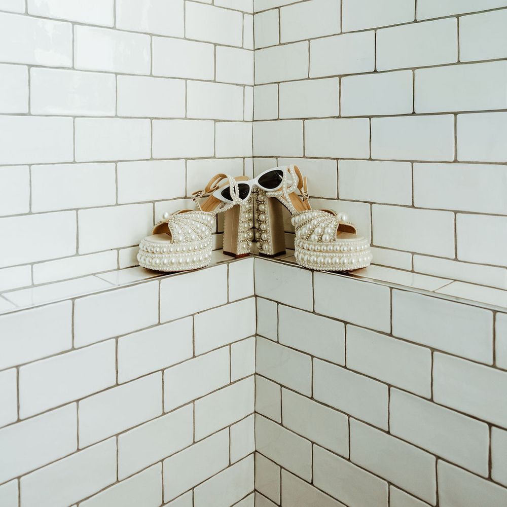 Pearl-embellished bridal platform sandals and white cat-eye sunglasses on a tiled ledge
