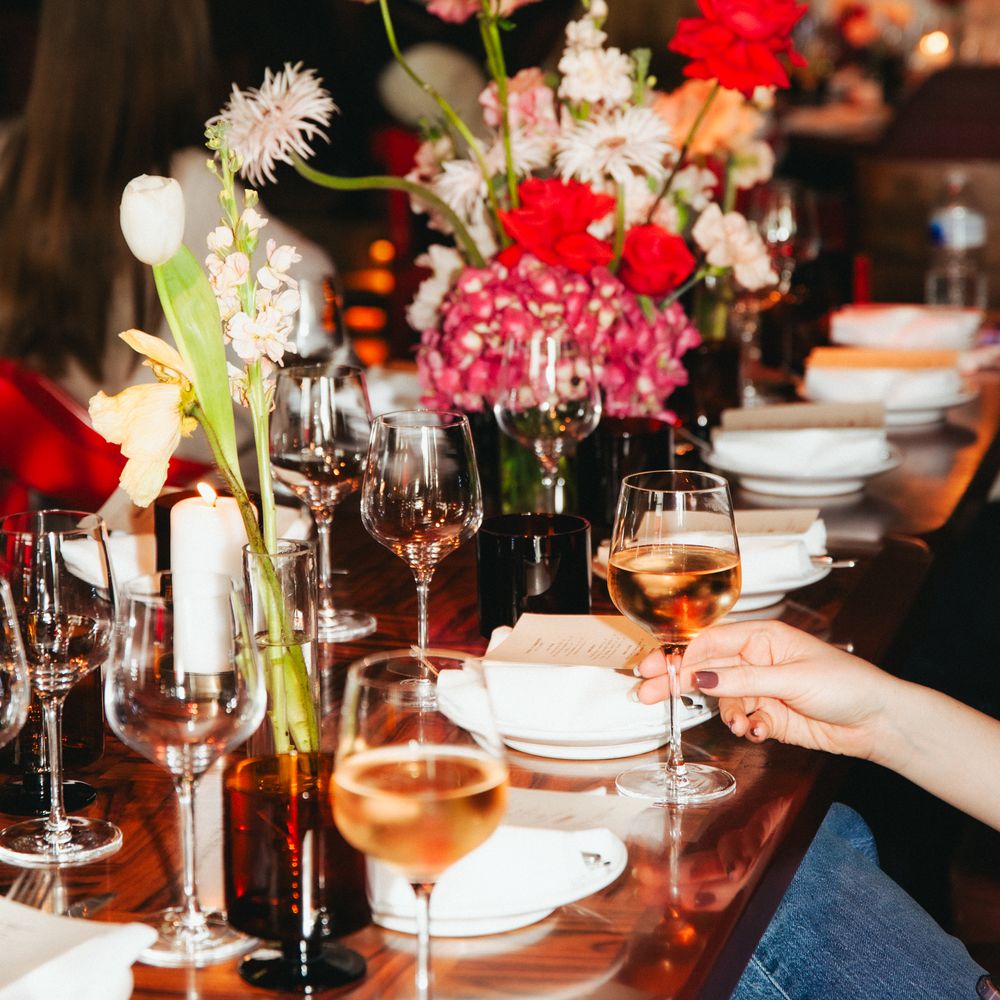 Guest reaching for white wine at a candlelit table with pink and red floral centrepieces