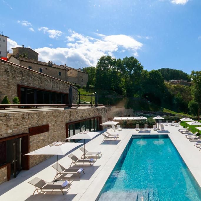 Outdoor pool lined with white parasols and sun loungers beside a stone building in the countryside