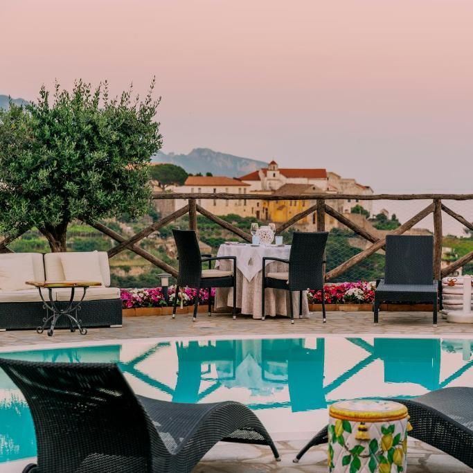 Poolside terrace at dusk with dining table, loungers and hilltop views over an Italian valley