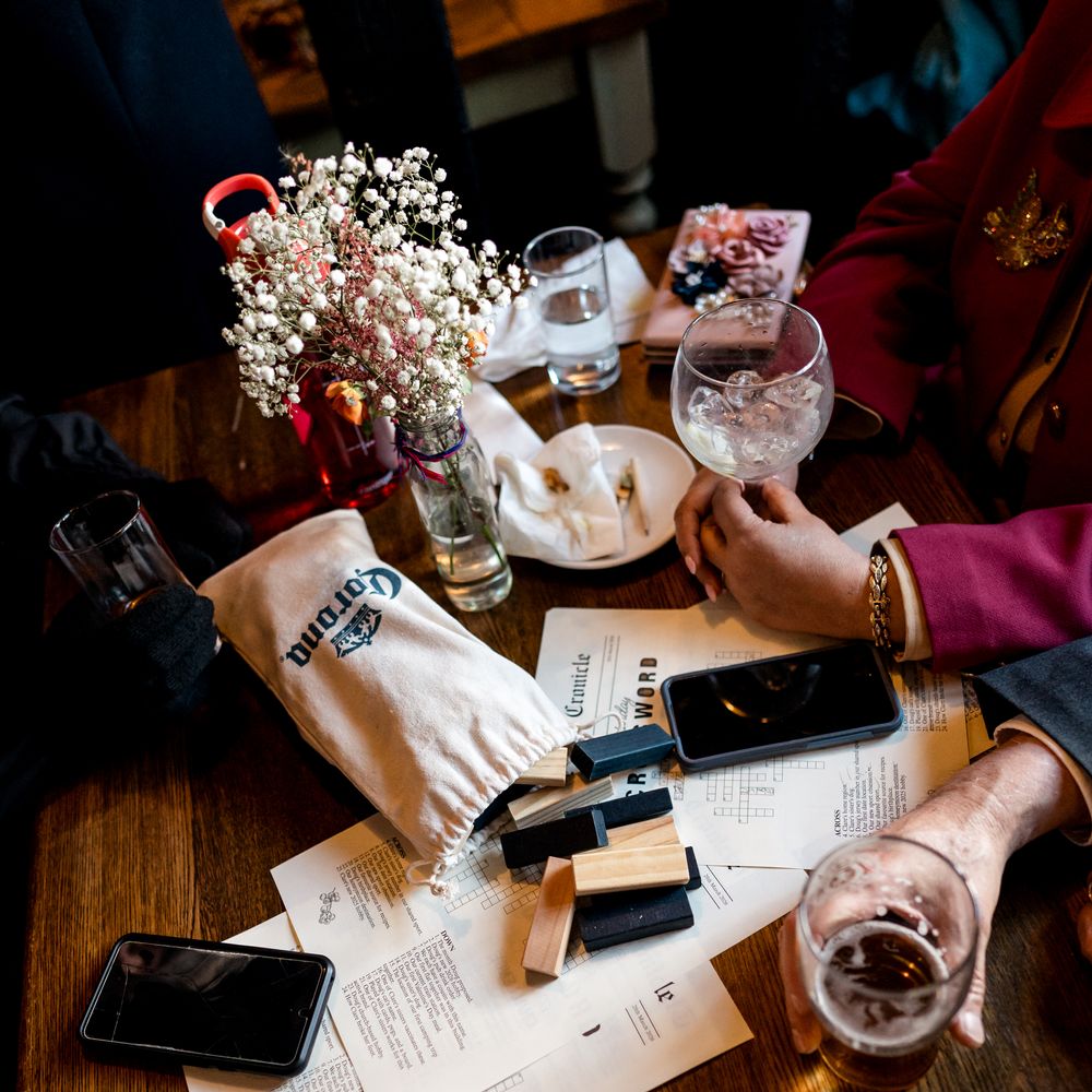 Guests gathered round a wooden pub table with drinks, gypsophila and a crossword game