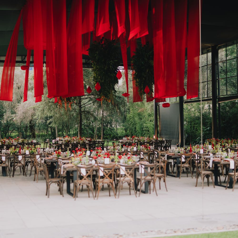 Outdoor reception with hanging red banners above rustic wooden tables and cross-back chairs