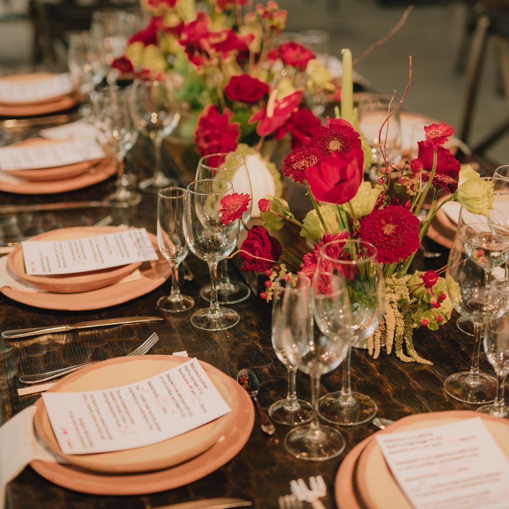 Rustic wooden table set with terracotta plates and vivid red floral centrepieces