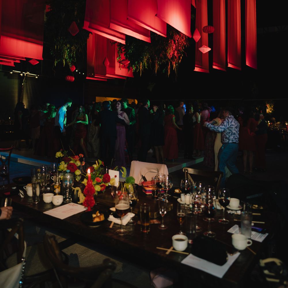 Guests dancing on a lit floor beside a candlelit banquet table under dramatic red lighting
