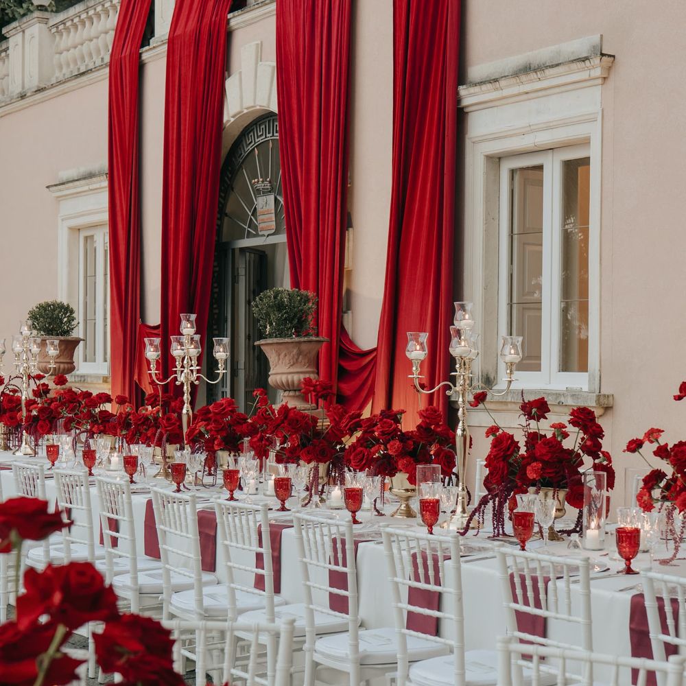 Outdoor banquet table with red roses, gold candelabra and white Chiavari chairs against a villa facade