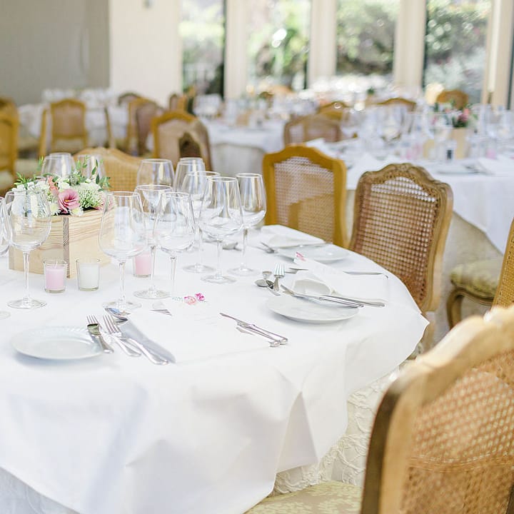 Round reception table set with white linen, crystal glassware and pastel floral centrepiece
