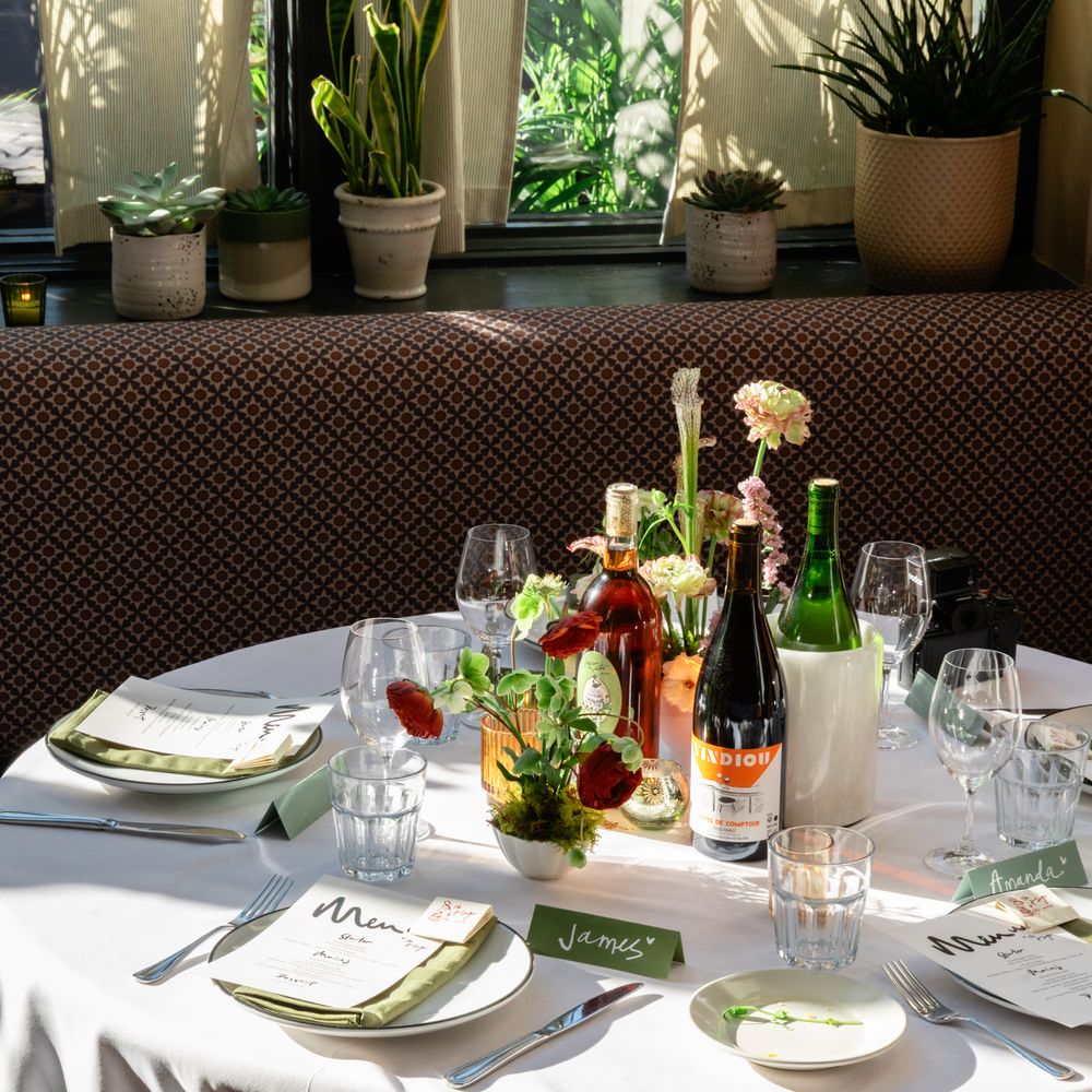 Round wedding table with white linen, sage napkins, wine bottles and small floral centrepiece