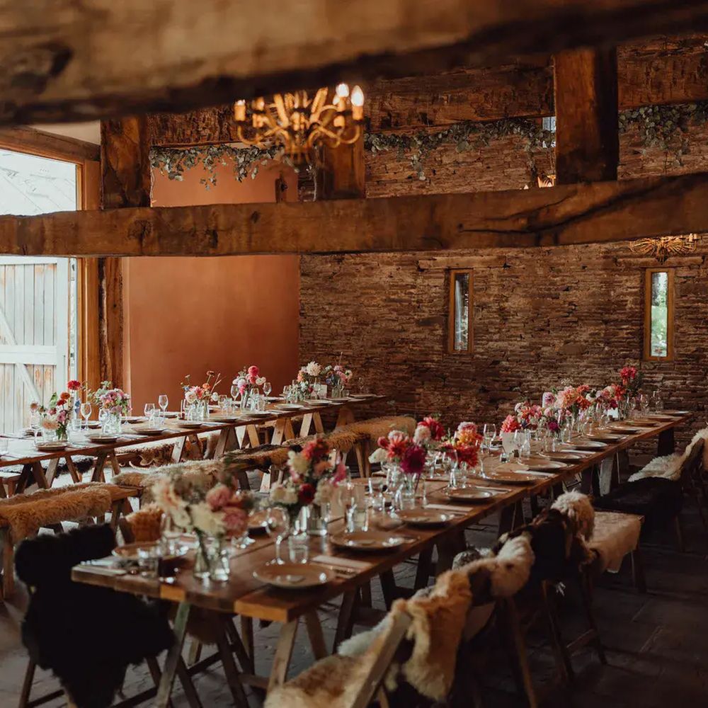 Rustic barn reception with trestle tables, sheepskin-draped benches and bright floral centrepieces