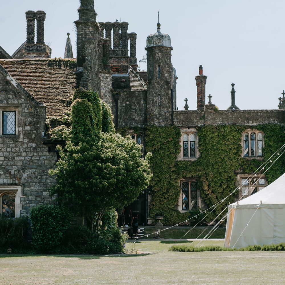 White sailcloth marquee on manicured lawns beside an ivy-clad Tudor manor house