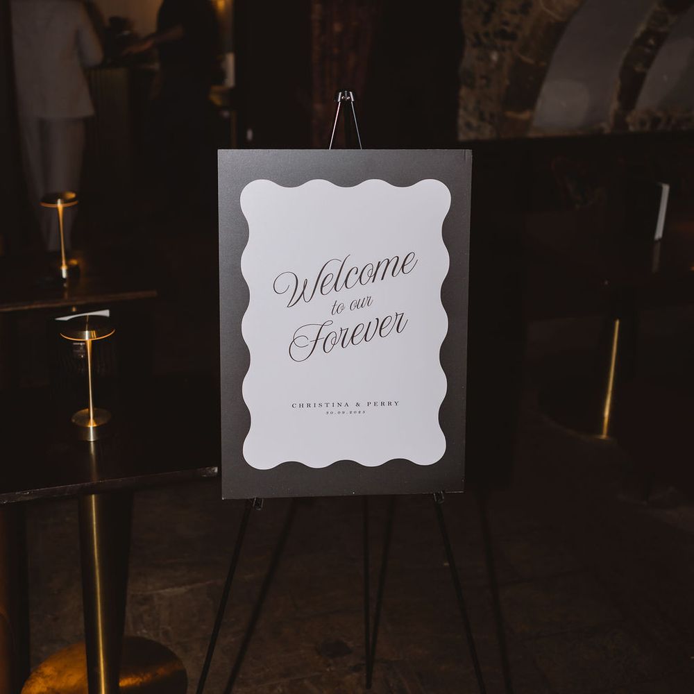 Scalloped welcome sign on an easel reading 'Welcome to our Forever' in a candlelit stone cellar