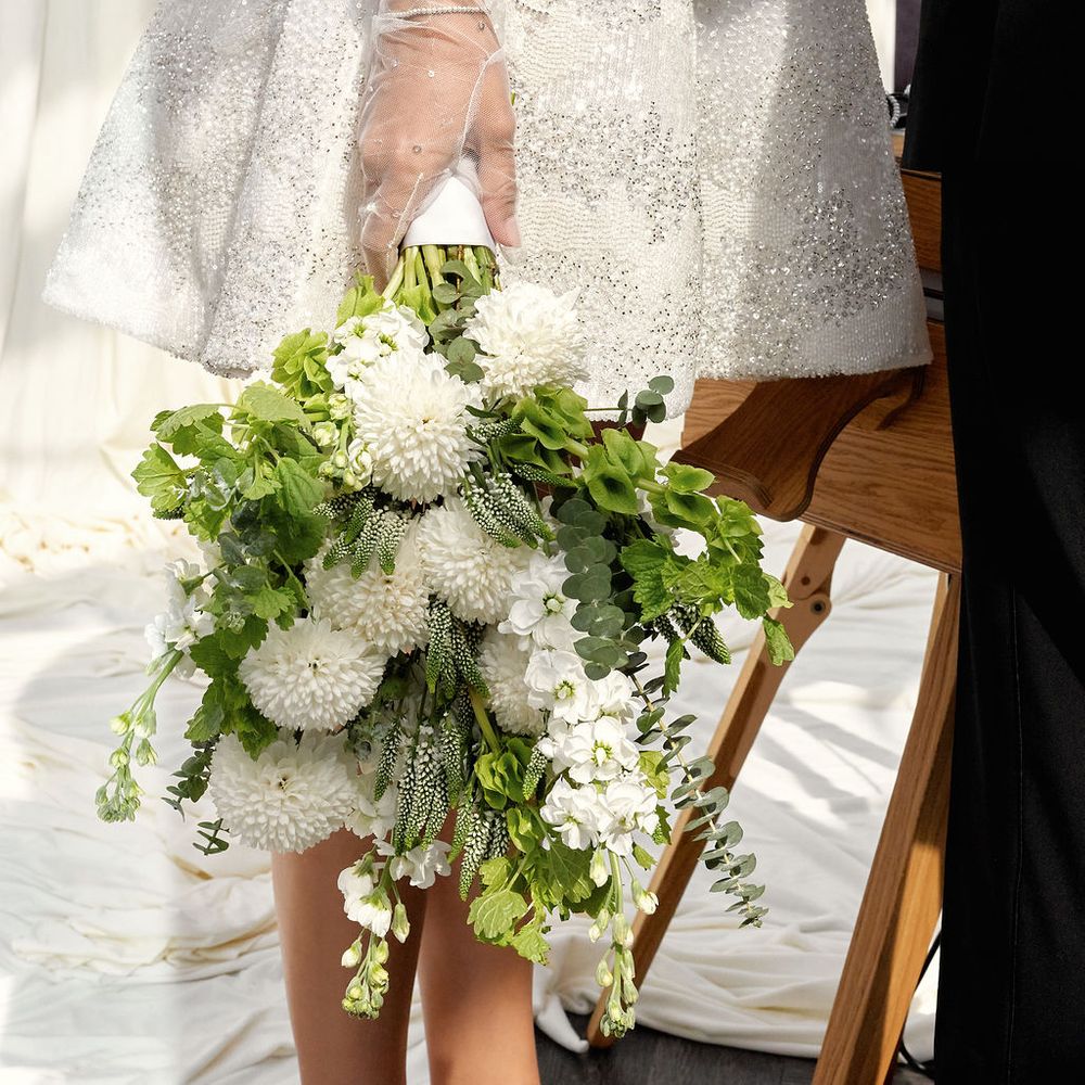 Bride in sequinned mini dress and sheer gloves holds a white and green trailing bouquet