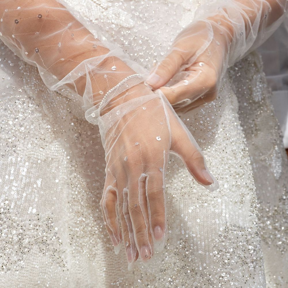 Bride's hands in sheer tulle gloves resting against a beaded sequinned wedding gown