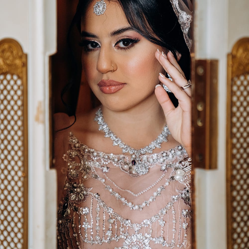 South Asian bride in beaded bridal wear with maang tikka and crystal necklace framed in a doorway
