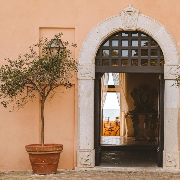 Arched stone doorway flanked by potted olive trees framing a sea view beyond
