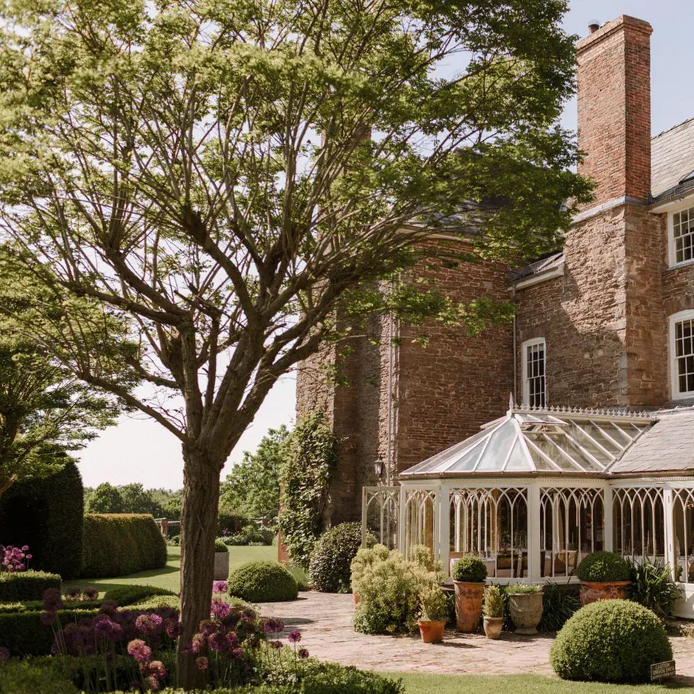 Stone country house with Victorian glass conservatory and manicured gardens with allium borders