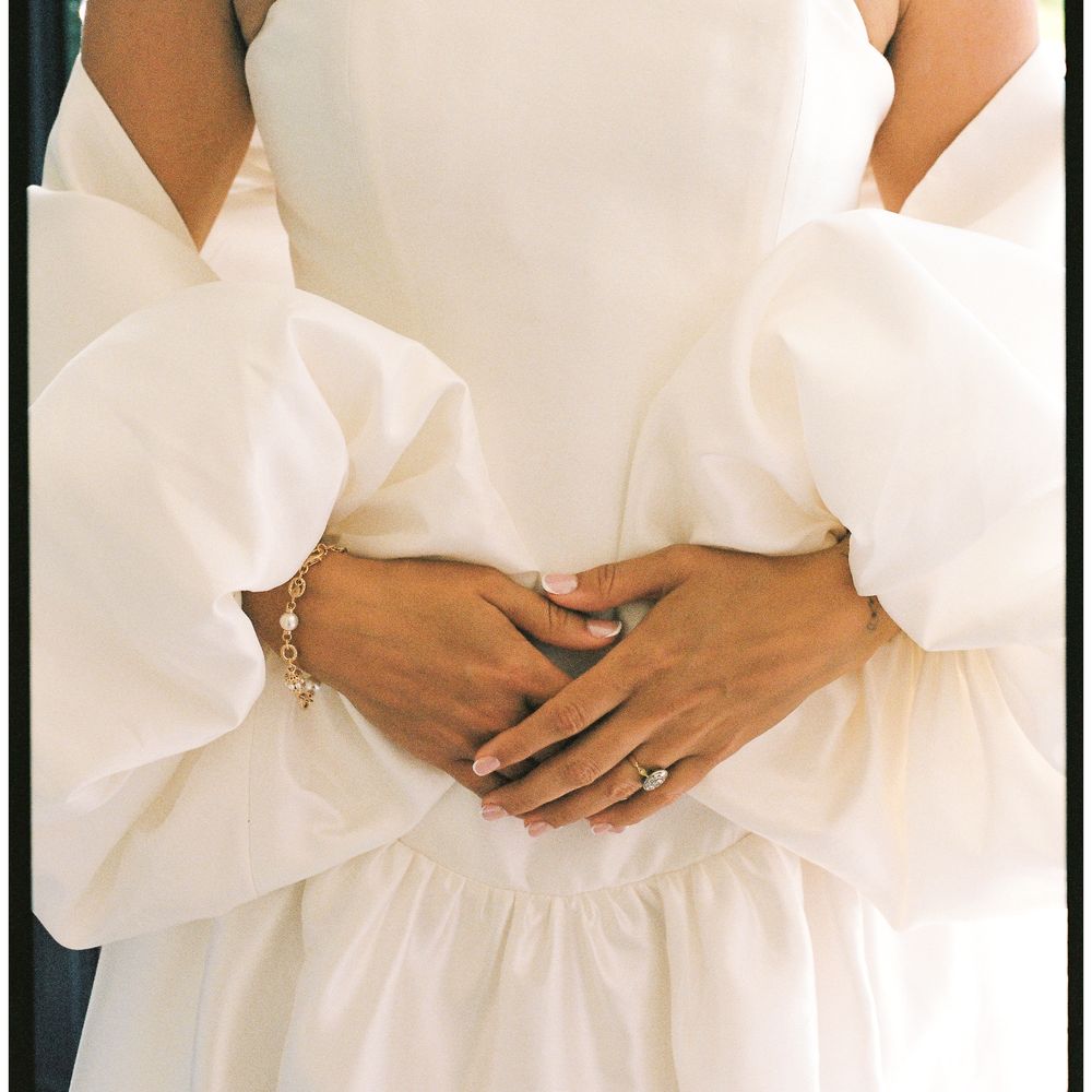 Bride in a strapless gown with dramatic puff sleeves, hands clasped showing pearl bracelet and ring