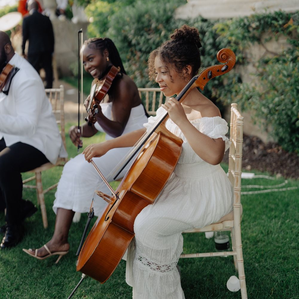 Cellist and violinist in white dresses playing outdoors on a manor house lawn