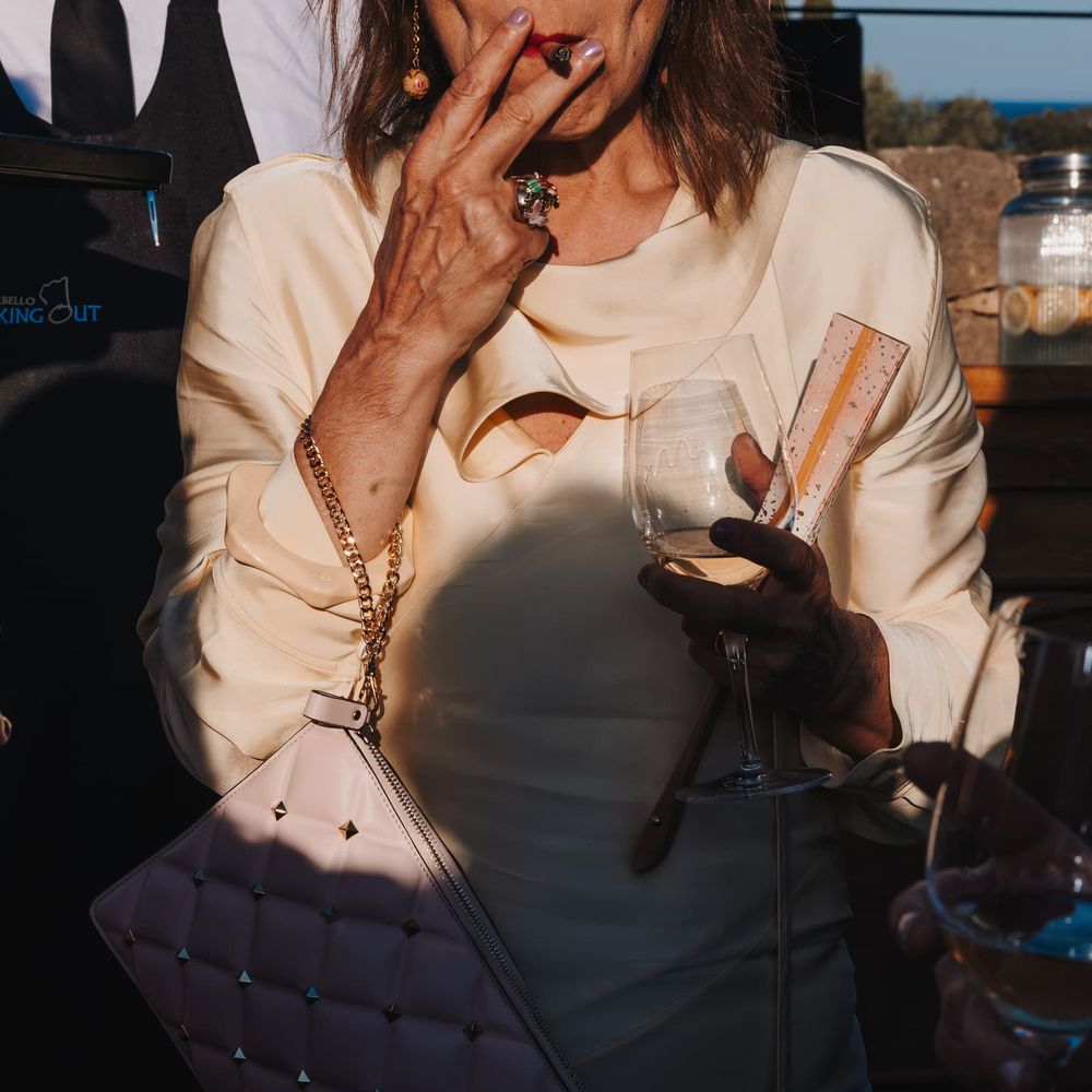 Guest in cream blouse holds a glass of white wine with a quilted studded clutch bag in golden light