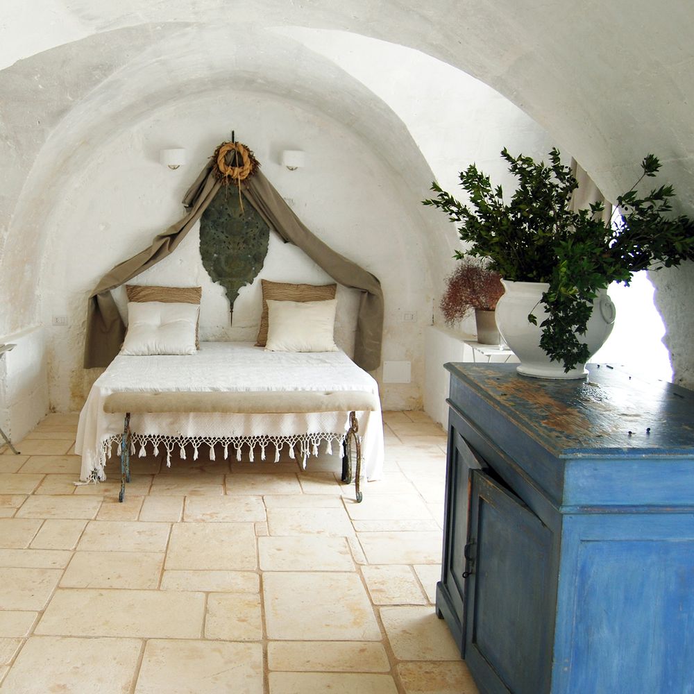 Rustic vaulted bedroom with whitewashed stone walls, tasselled bedspread and blue painted cabinet