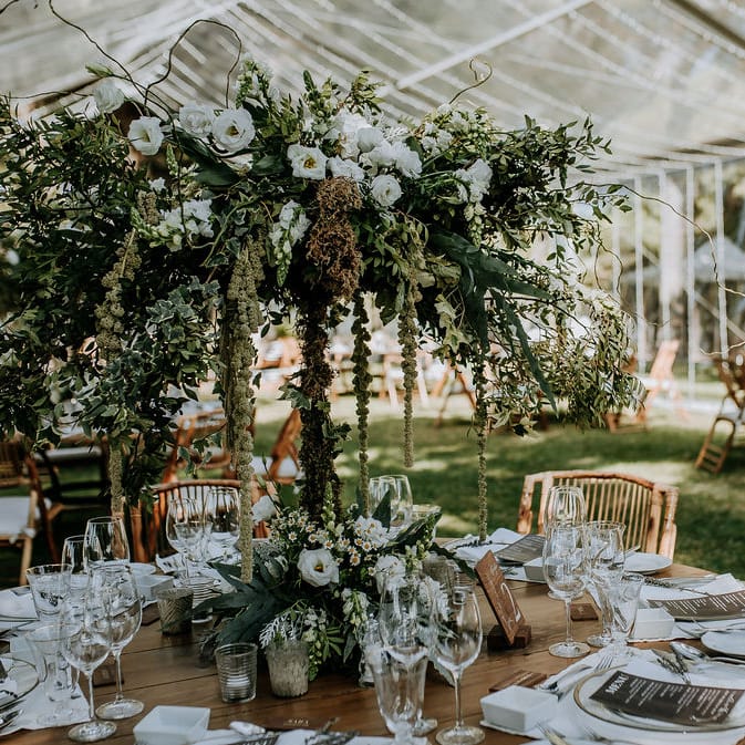 Tall foliage and white bloom centrepiece on a wooden table under a clear marquee