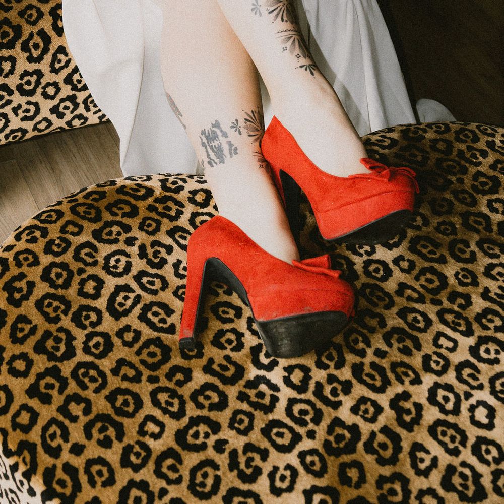 Tattooed bride's legs in red suede platform heels resting on a leopard-print armchair
