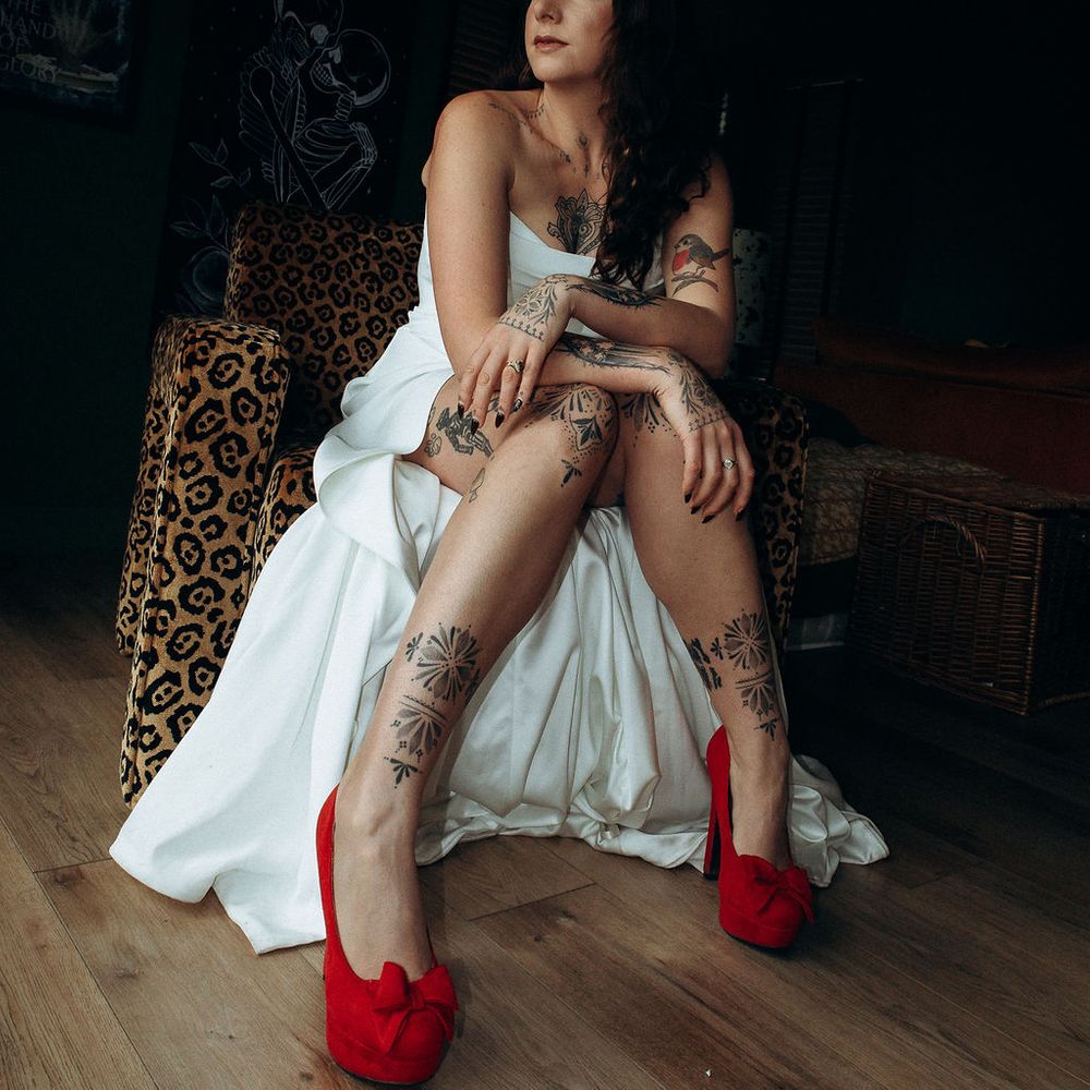 Tattooed bride in a strapless gown and red heels seated on a leopard-print chair