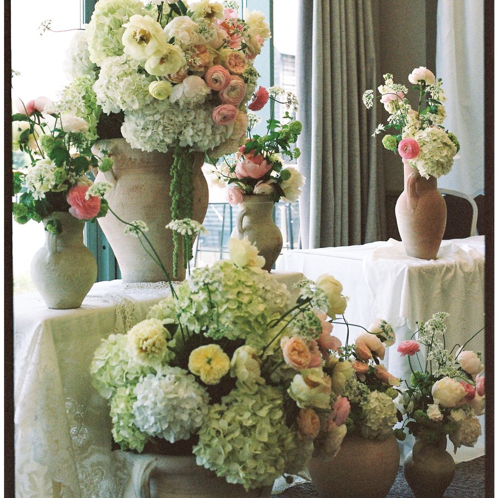 Terracotta urns filled with hydrangeas, roses and ranunculus arranged by a curtained window