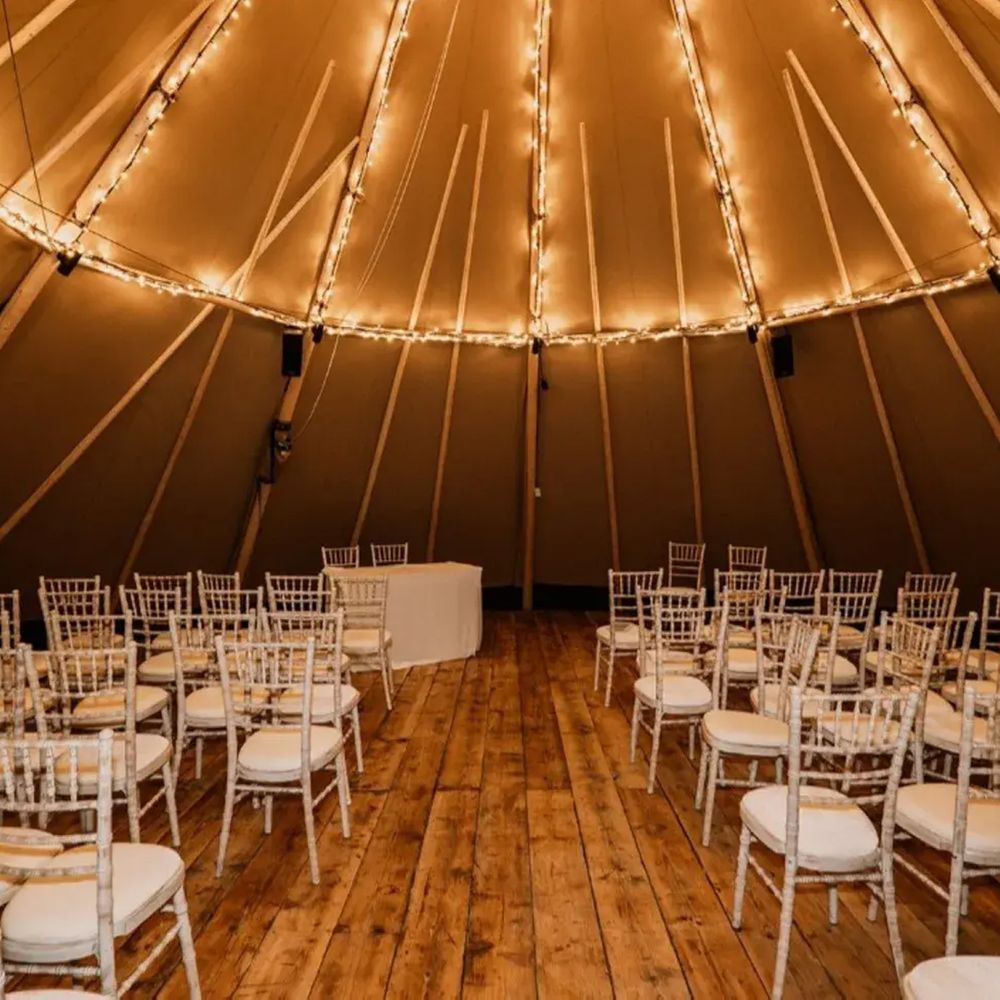 Tipi wedding ceremony set with white Chiavari chairs and fairy lights on wooden flooring