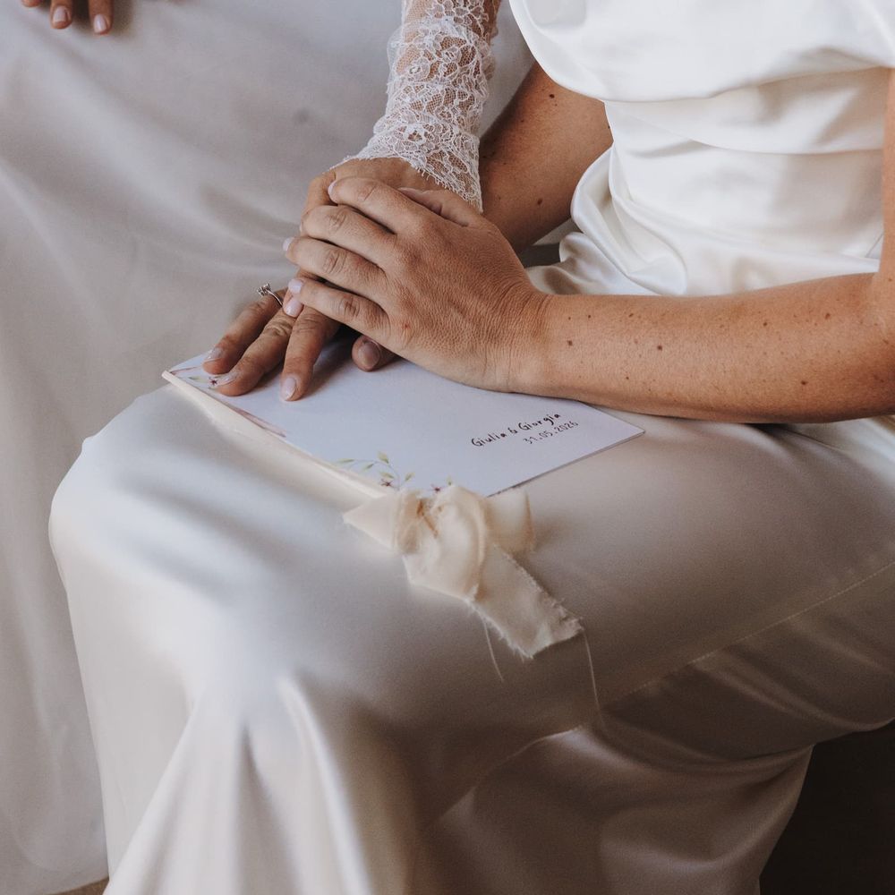 Two brides in ivory gowns hold hands over a personalised booklet tied with silk ribbon