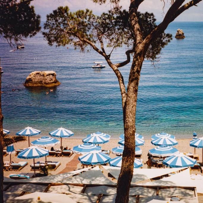 Blue and white striped parasols dotted across a sandy beach beside clear turquoise sea