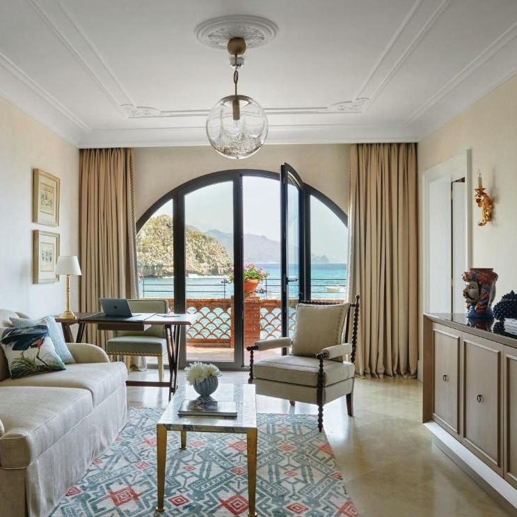 Elegant hotel suite sitting room with sofa, armchair and arched doors opening to a sea view balcony